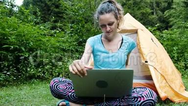 女游客自由职业者在露营地打开一台笔记本电脑，在旅游帐篷的背景下在大自然中工作。